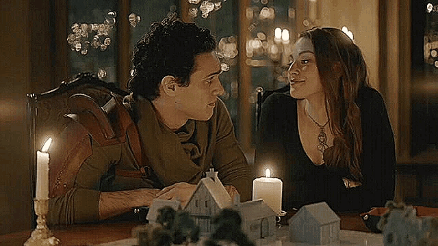 a man and woman are sitting at a table with candles .