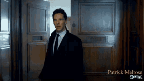 a man in a suit and tie is standing in front of a door that says patrick melrose showtime on it