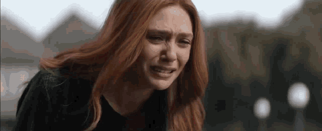 a close up of a woman with red hair crying in a park .