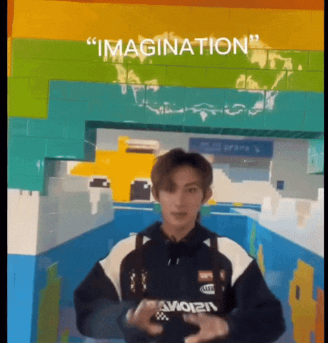 a young man is standing in front of a wall with the word imagination on it .