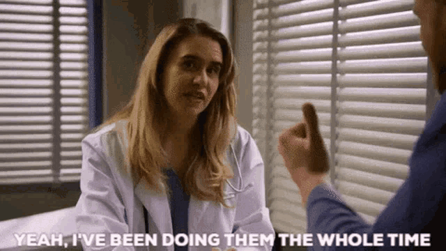 a woman in a lab coat is talking to a man in a hospital bed and giving him a thumbs up .