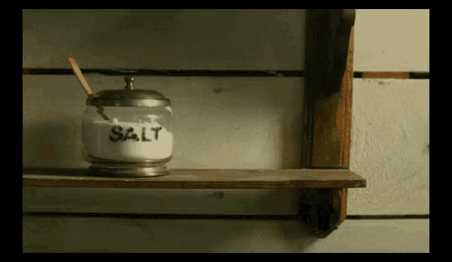 a jar of salt sits on a shelf with a spoon