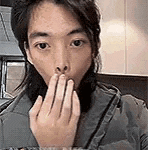 a man is covering his mouth with his hand while looking at the camera .