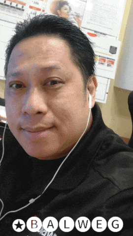 a man wearing ear buds and a balweg shirt looks at the camera