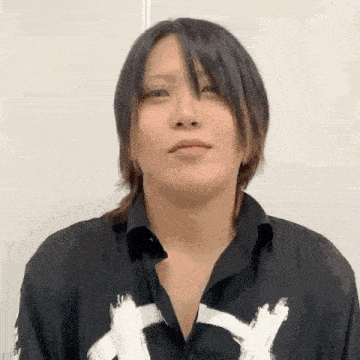 a young man with long black hair is wearing a black shirt with white letters on it .