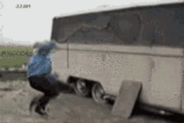 a man in a blue jacket is jumping over a trailer