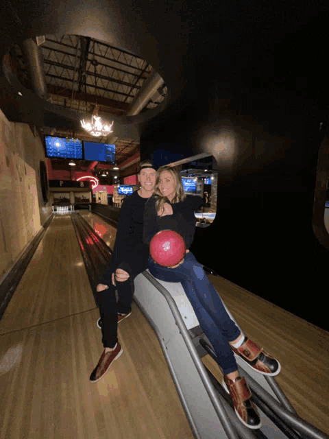 a man and a woman sitting on a bowling alley holding a bowling ball
