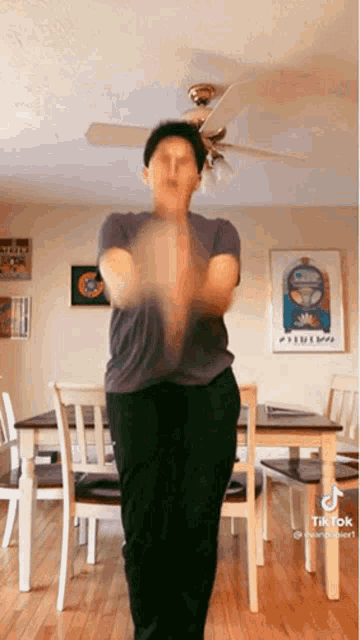 a man is dancing in a living room with a ceiling fan and a table and chairs .