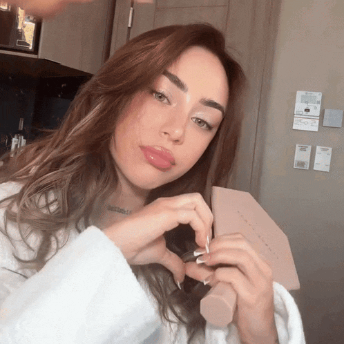 a woman in a white robe is holding a fenty beauty brush