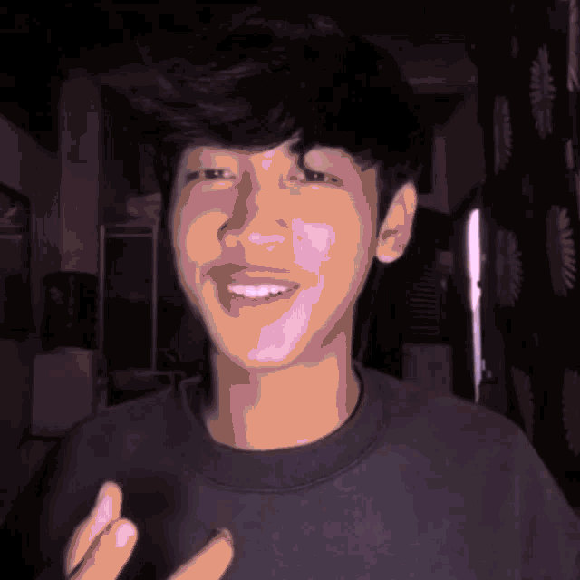 a young man wearing a black shirt is smiling and making a gesture with his hands
