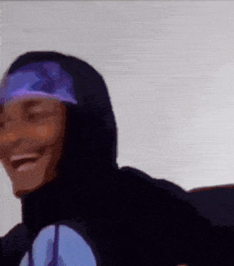 a person wearing a black hoodie and a purple headband is smiling