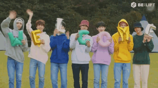 a group of young men are standing in a field holding balloons in the shape of the letter g .