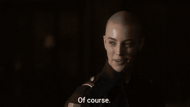 a woman with a shaved head says of course in a dark room