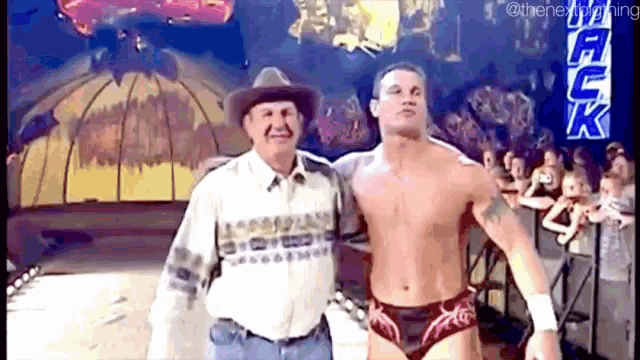 a man in a cowboy hat is standing next to a shirtless wrestler .