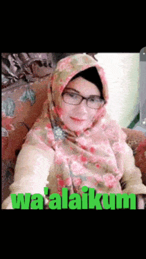 a woman wearing a hijab and glasses sits in a chair with the words wa ' alaikum written in green