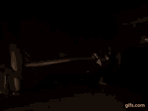 a woman is holding a gun in a dark room and pointing at the camera .
