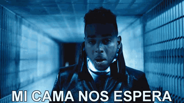 a man in a black jacket stands in a dark hallway with the words mi cama nos espera above him
