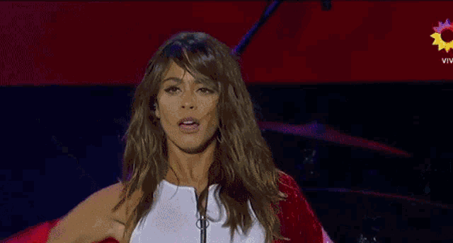 a woman in a red jacket is standing on a stage with her arms outstretched in front of a microphone