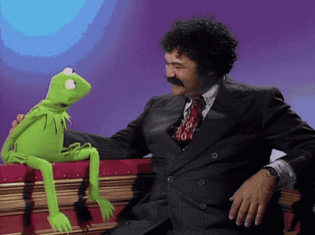 a man in a suit is sitting next to a kermit the frog puppet