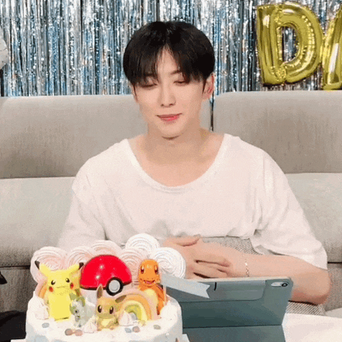 a man is sitting in front of a cake with pokemon on it and a tablet .