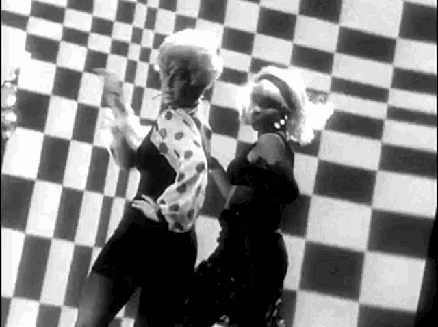 a black and white photo of two women dancing in front of a checkered wall .