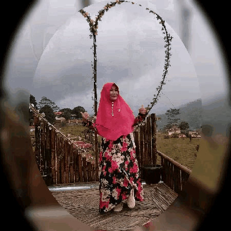 a woman wearing a pink hijab and a floral dress gives a thumbs up