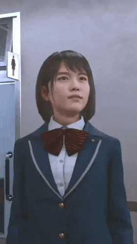 a girl in a school uniform and bow tie is standing in front of a toilet .