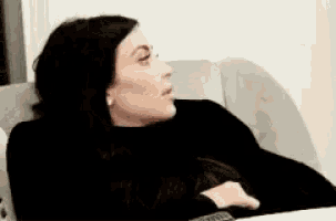 a woman is sitting on a couch holding a remote control and looking at something .