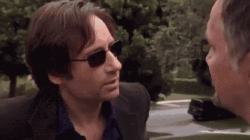 a man in a suit and sunglasses is talking to another man .