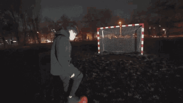 a man in a black jacket is kicking a soccer ball at a goal