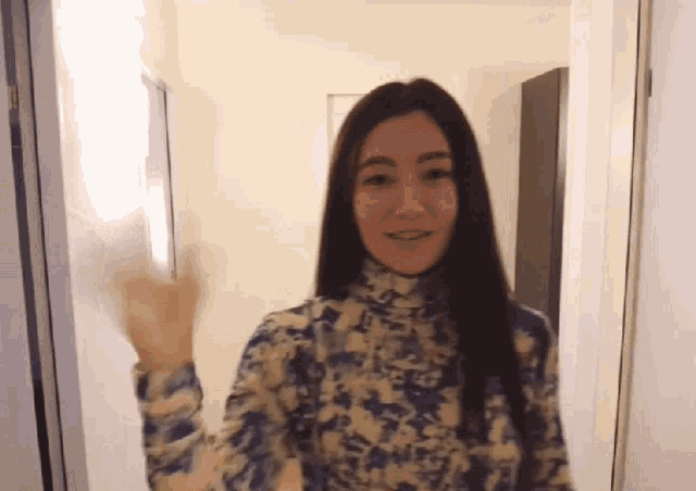 a woman in a blue and white floral shirt is waving at the camera