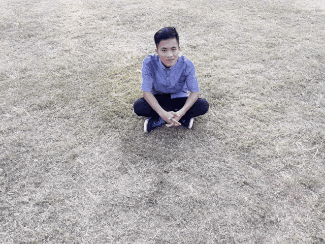 a young man is sitting in the grass with his legs crossed