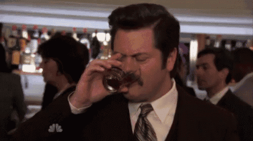 a man in a suit and tie is drinking a glass of whiskey in a bar .