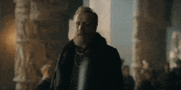 a man with a beard is standing in front of a group of people in a room .