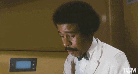 a man in a white suit and bow tie is standing in front of a screen that says tom