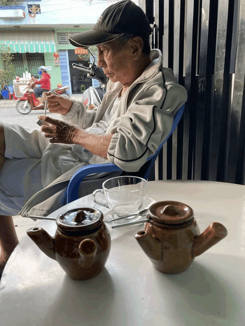 a man sits at a table with two teapots and a cup