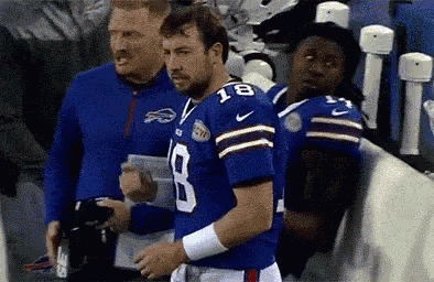 a football player wearing a blue jersey with the number 18 on it is standing next to a coach .