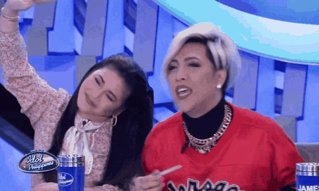 two women sitting at a table with idol philippines written on the front