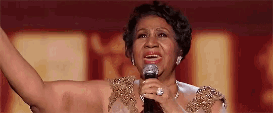 a woman is singing into a microphone while wearing a gold dress .