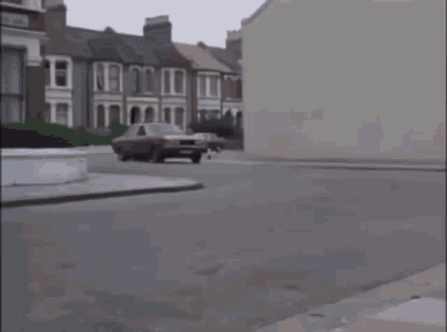 a red car is driving down a street in front of a building .