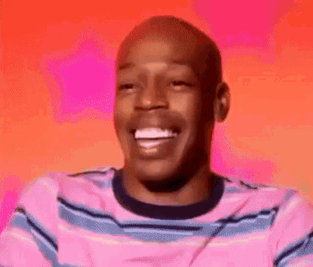 a man in a pink and blue striped shirt is laughing with his eyes closed .