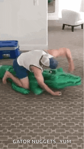 a man is kneeling on the floor playing with a crocodile costume .