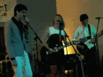 a man singing into a microphone while a woman plays guitar