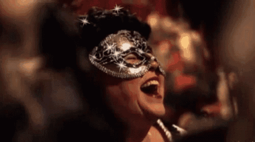 a woman is wearing a carnival mask and laughing with her mouth open .