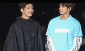 two young men are standing next to each other in a dark room . one of the men is wearing a blue shirt .
