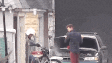 a man is standing next to a motorcycle and a car with the hood up .