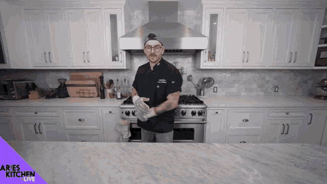 a man in a chef 's uniform is standing in a kitchen with aries kitchen live written on the counter