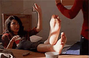 a woman is sitting at a table with her feet up and a man is standing behind her holding a video game controller .