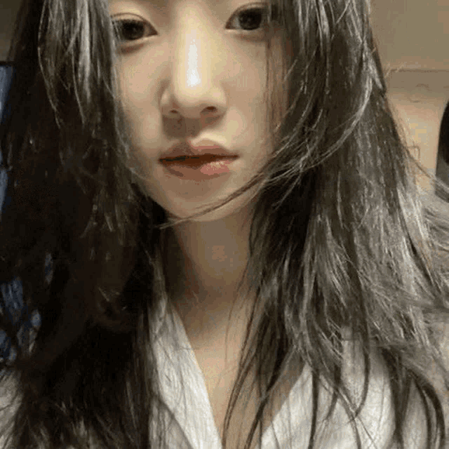 a close up of a woman 's face with long black hair and a white shirt .