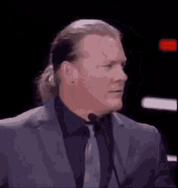 a man in a suit and tie is talking into a microphone in a dark room .